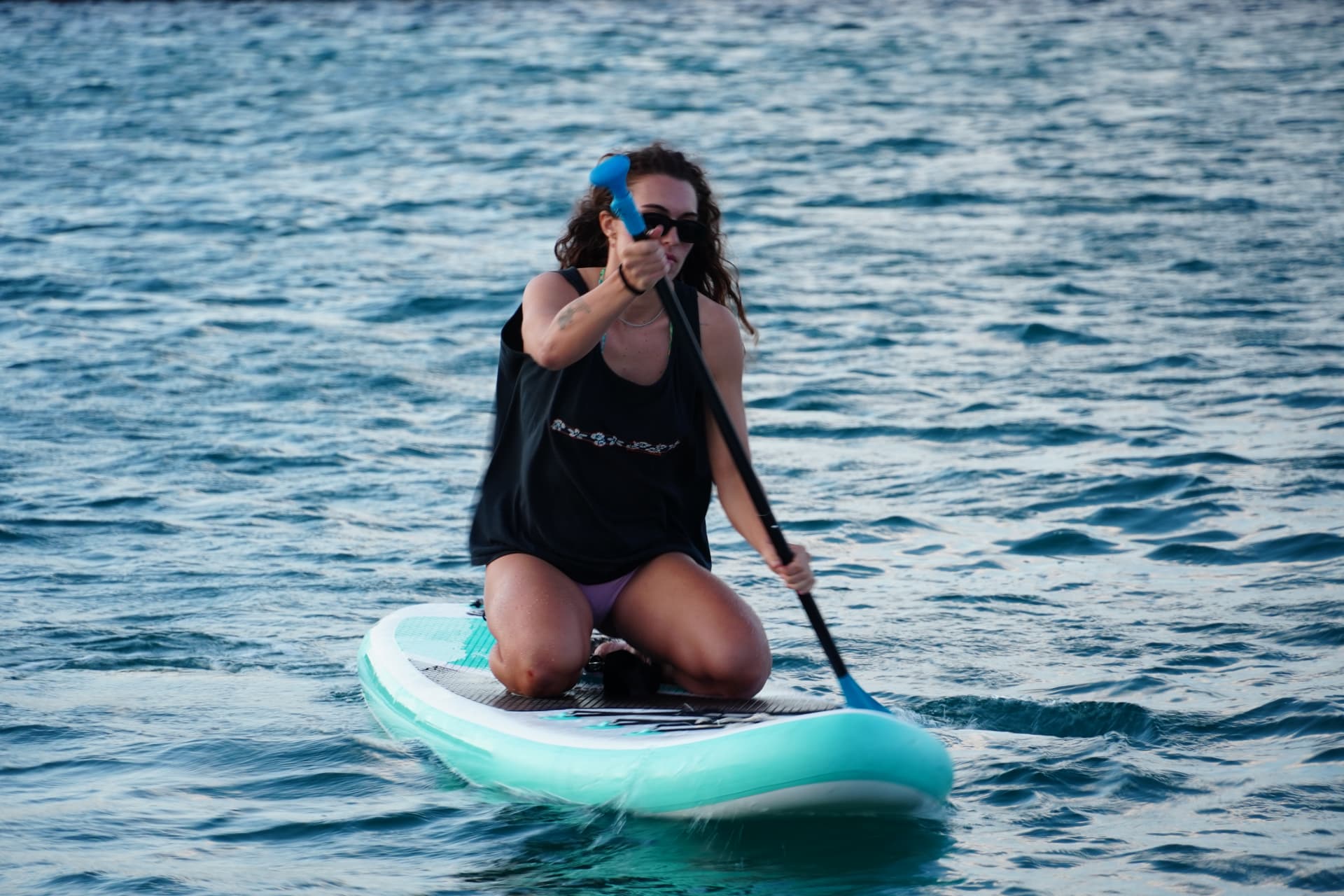 A guest paddling kneeling on a turquoise board in the bay