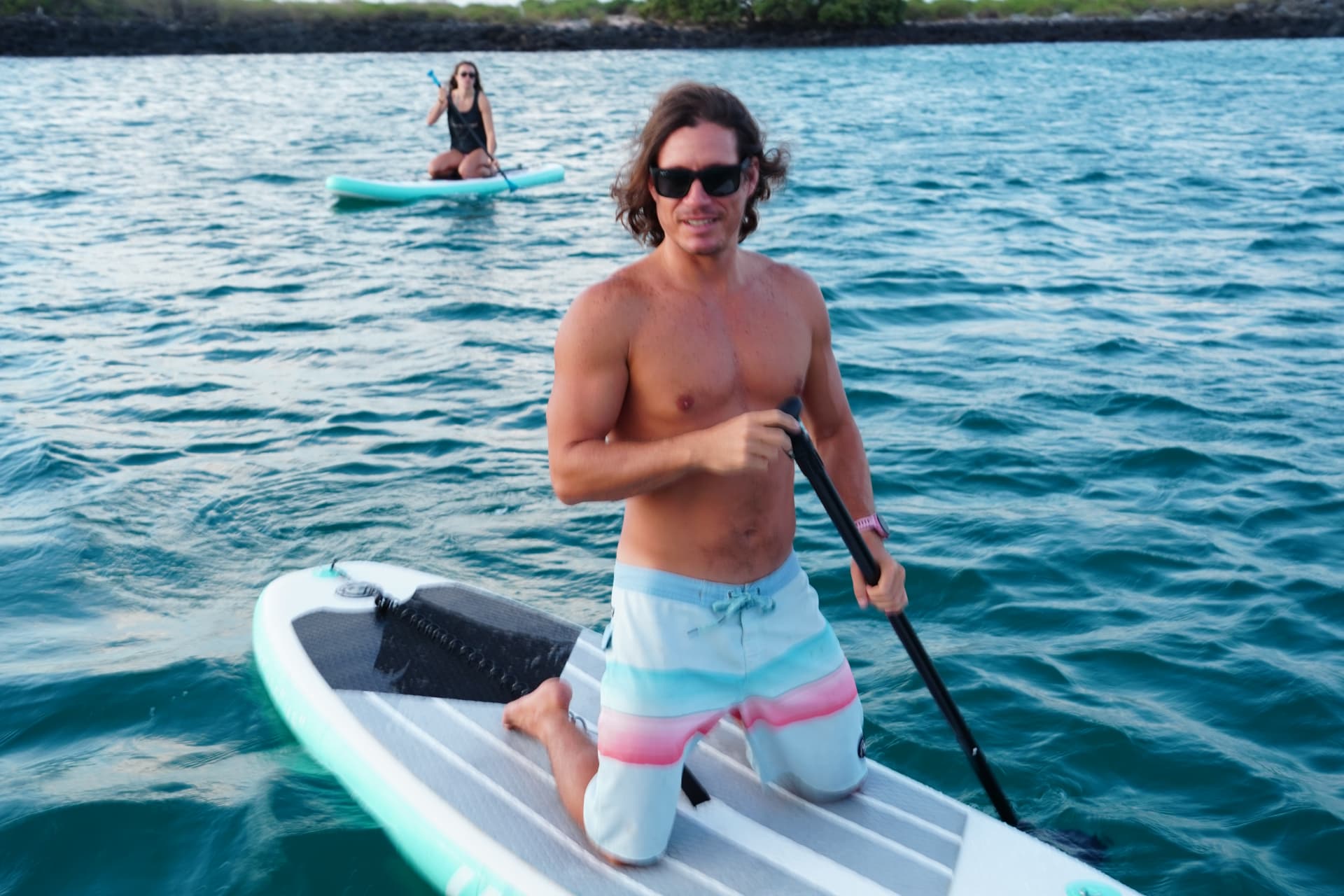 A guest kneeling on a paddleboard in clear blue water