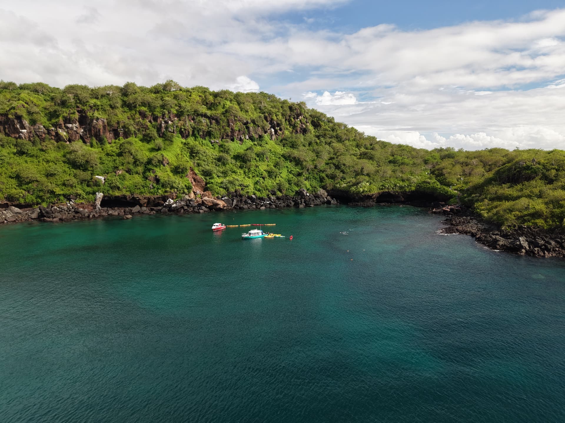 Aerial view of boats and kayaks in a turquoise bay beneath a green hillside